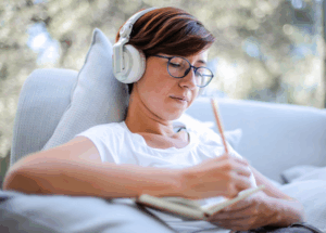 Woman wearing headphones and writing notes on paper